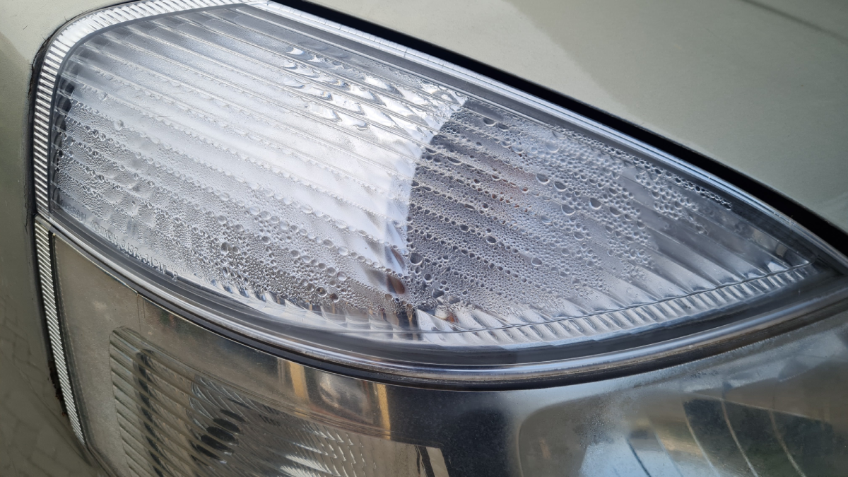 An upclose image of a car with foggy headlights, highlighting the moisture droplets inside