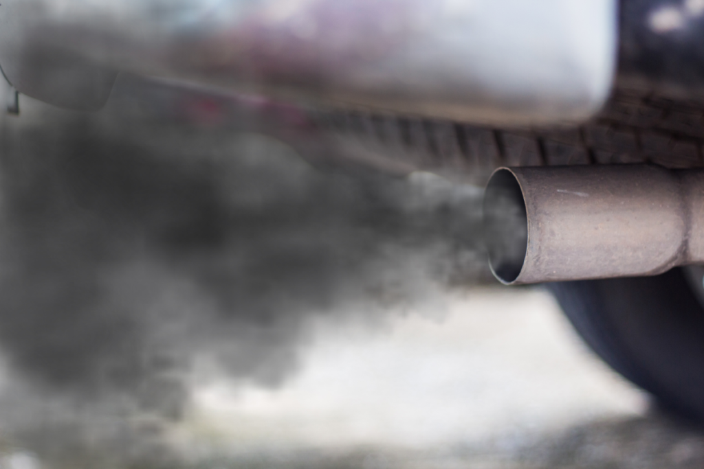 An upclose image of a car's exhaust pipe smoking black smoke into the air