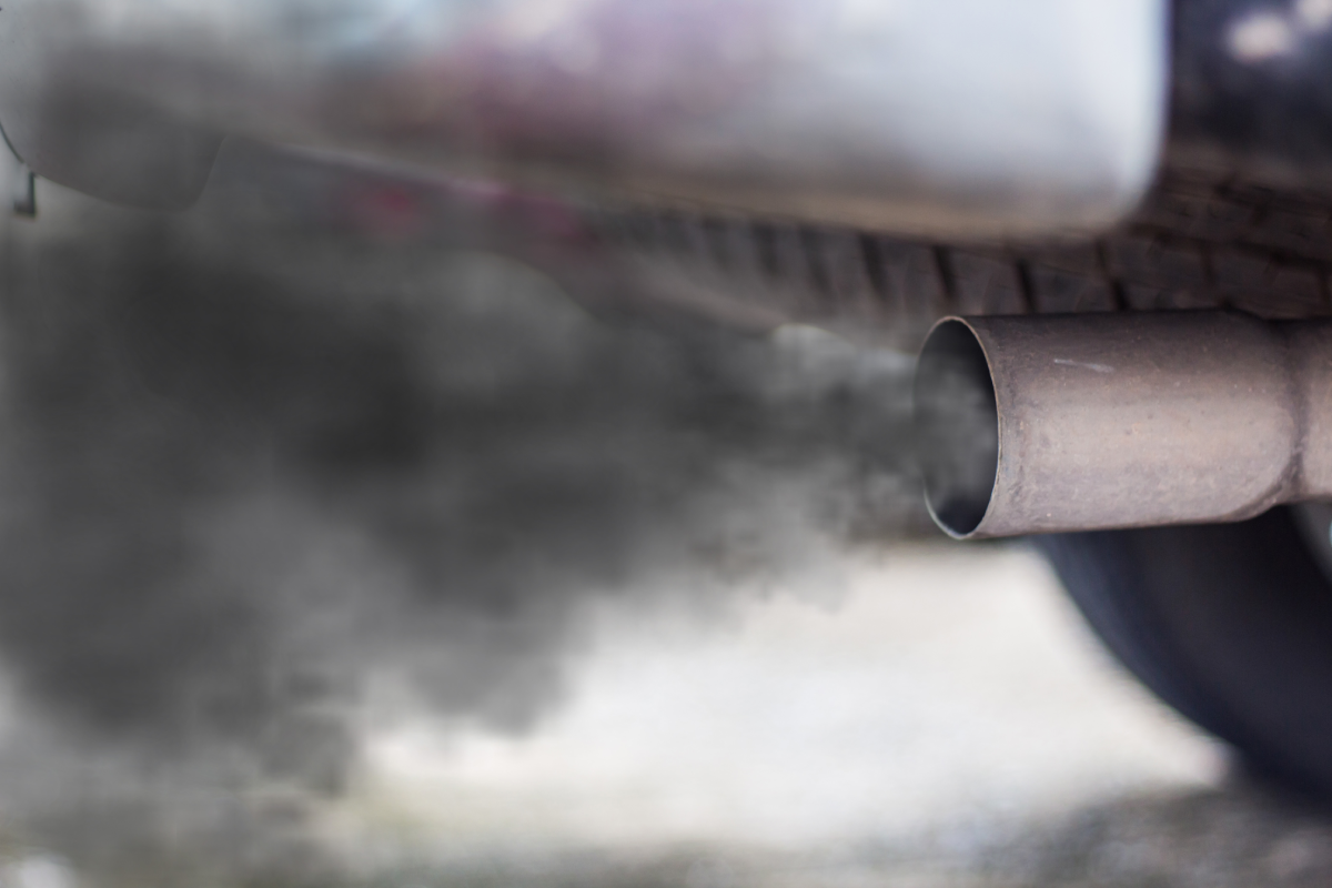 An upclose image of a car's exhaust pipe smoking black smoke into the air